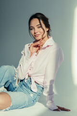 Young woman in ripped jeans and shirt sits sunlit.