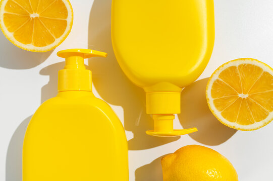 Yellow plastic cosmetic bottles, fresh whole lemon and halves on white background flat lay top view. Organic natural cosmetics with lemon extract. Moisturizing soap, cream, body lotion, sunscreen