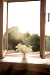 Open vintage wooden window with a bouquet of flowers during a sunny summer morning. 