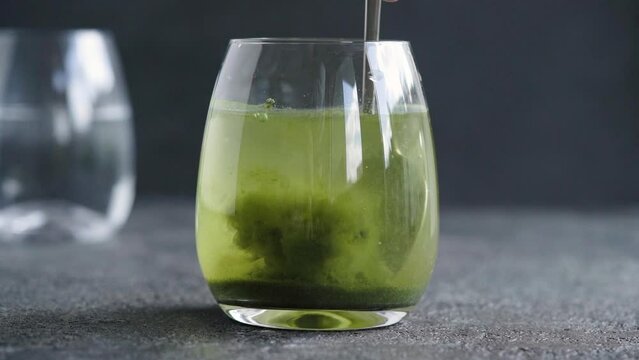 Stirring green barley grass powder in a glass of water - preparation of a healthy drink
