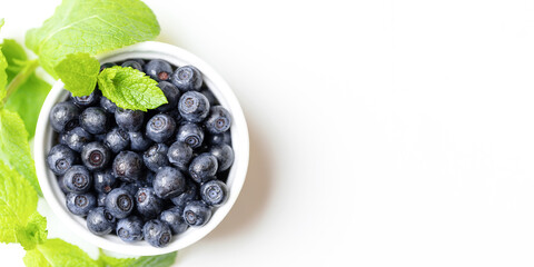 White bowl with wild blueberries and fresh green mint leaves on white. Banner. Top view. Copy space.