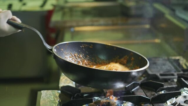 Chef is tossing spaghetti with tomato sauce on a pan. Slow motion. 4K. Close up.
