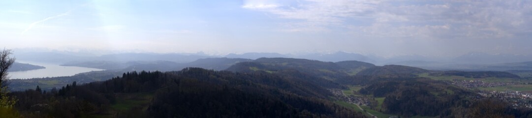 Fototapeta premium Wide angle panoramic view from local mountain Uetliberg with Lake Zürich and Swiss Alps in the background on a blue cloudy spring day. Photo taken April 14th, 2022, Zurich, Switzerland.