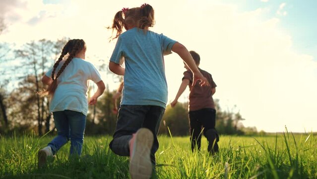 kids run in the park. a large group of a team of children running back view sunlight in the summer on the grass in the park camera movement. people in the park happy family kid dream concept lifestyle