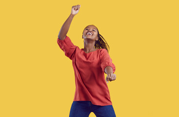 Excited millennial African American girl isolated on yellow studio background dancing listening to...