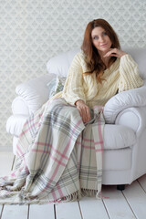 Young beautiful woman with blanket sitting in armchair