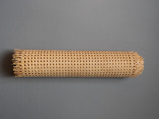 Rouleau de cannage en rotin naturel posé sur fond gris, matériau artisanal utilisé pour la décoration, le mobilier ou la rénovation de chaises