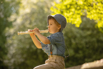Stylishly dressed child, boy with pet dog, playing in the park on flute