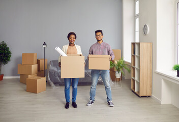 Fototapeta na wymiar Portrait of happy multiethnic family buyers with boxes excited to move into new apartment together. Smiling multiracial couple renters relocate to own house or home. Real estate, rent concept.