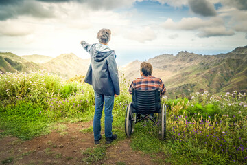 Young man and his wife in wheelchair travelling together in mountains