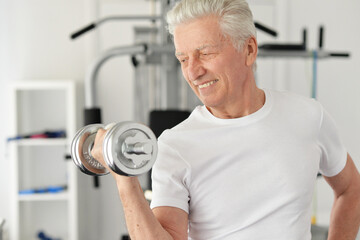 Portrait of elderly man with dumbbell in a gym during exercise