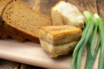 Homemade smoked lard on a wooden board with black bread and green onions.