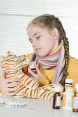 Sick girl with toy tiger sitting at table with medicine at home