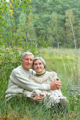 Portrait of happy senior couple sitting by pond