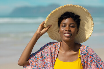 Portrait of smiling african american young woman wearing hat standing against sea on sunny day