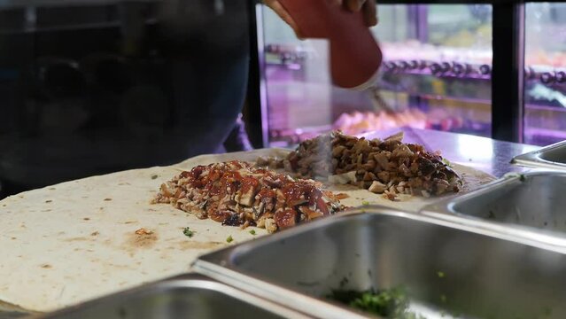hands of a male cook pour sauce and mayonnaise into a doner kebab in the process of cooking. Shawarma with meat and vegetables in Armenian lavash. Fast food harm concept