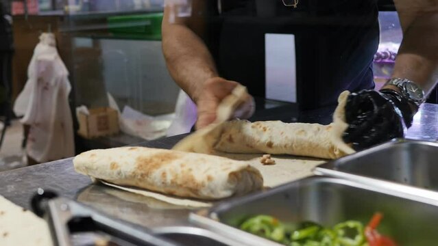 the male hands of a restaurant chef wrap the ingredients in pita bread in the process of cooking doner kebab. The cook in one glove rolls up cooking shawarma with meat and vegetables