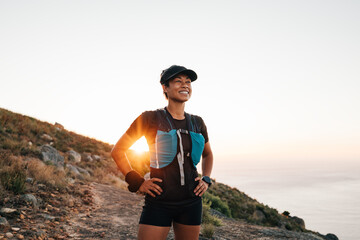 Portrait of sporty woman with cap relaxing at sunset. Female taking break on trail run.