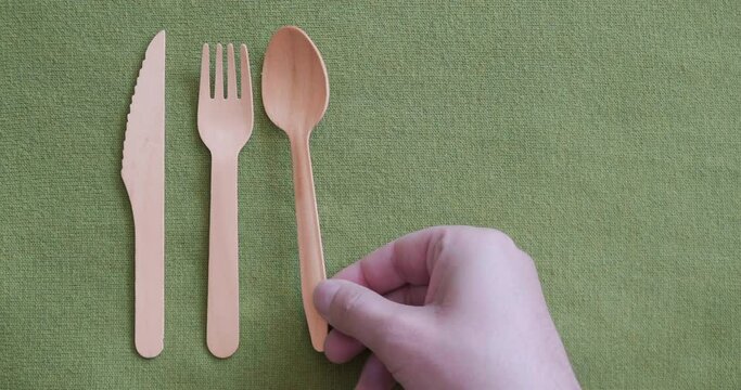 Eco friendly disposable takeaway wooden cutlery (knife, fork, spoon) on green fabric with copy space. Ethical, plastic free, biodegradable.
