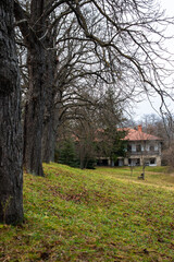 Autumn landscape with the house in the park, bare trees all around and lonely bench nearby 