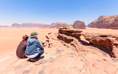 one tourist with his local guide looking at the stone arch in the desert of wadi rum in Jordan....