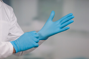 Close-up of hands putting on medical gloves in front of a clinic/ICU room 