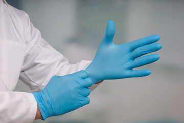 Close-up of hands putting on medical gloves in front of a clinic/ICU room 