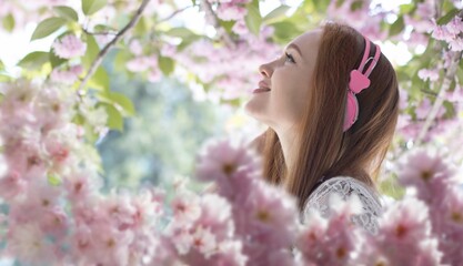 Fototapeta premium beautiful girl with headphones among sakura flowers, background 