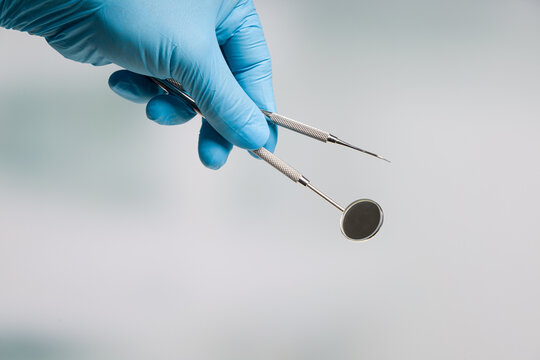 Close-up of dentist's hand in blue gloves presenting dental instruments for prophylaxis examination