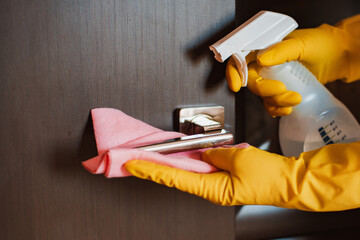 Close-up view of a woman hand in a yellow glove using a napkin to disinfect and clean the door...