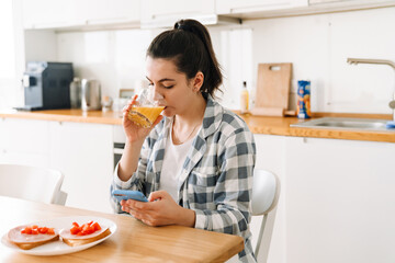 Young woman using mobile phone while having breakfast