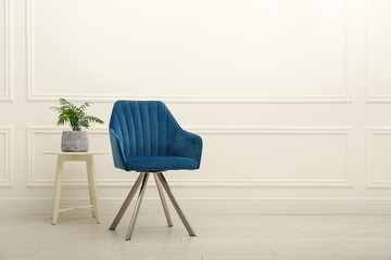 Modern blue armchair and houseplant on wooden table near white wall indoors. Space for text