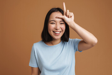 Young asian woman wearing t-shirt laughing and pointing finger upward