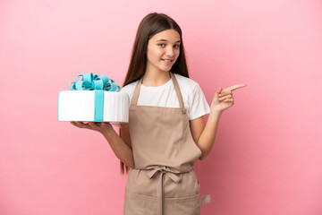 Little girl with a big cake over isolated pink background pointing finger to the side