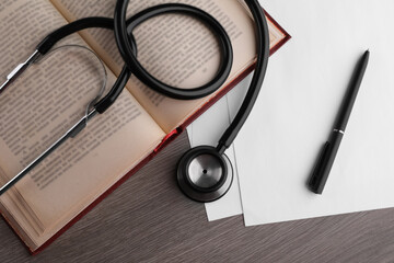 Book, stethoscope, pen and paper on wooden table, flat lay. Medical education