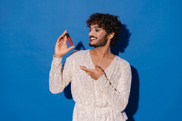 Young curly man with makeup smiling and showing lipstick