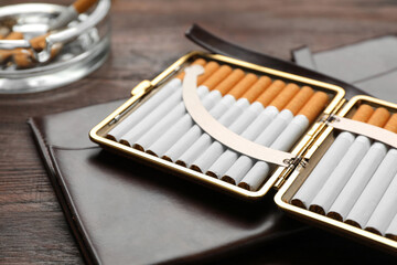 Open case with tobacco filter cigarettes and clutch on wooden table, closeup