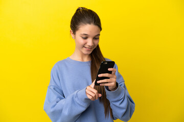 Little girl over isolated yellow background sending a message or email with the mobile