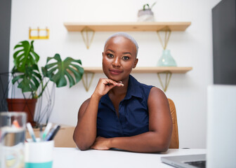 A young Black businesswoman poses for the camera at her office desk