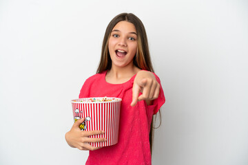 Little girl over isolated white background holding a big bucket of popcorns while pointing front