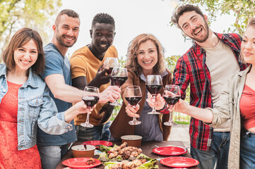 Cheerful friends drinking red wine outside  - Colleagues toasting together during social activities organized by working company- multigenerational friendship concept. - obrazy, fototapety, plakaty