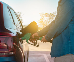 Detalle de hombre caucásico, repostando con la manguera de gasolina, con rayo de sol, en la...