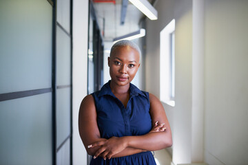 A powerful Black businesswoman poses with arms folded in office corridor