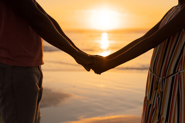 Midsection of african american young couple holding hands and standing against sea and sky at sunset