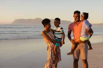 Happy african american young parents carrying son and daughter while standing against sea and sky