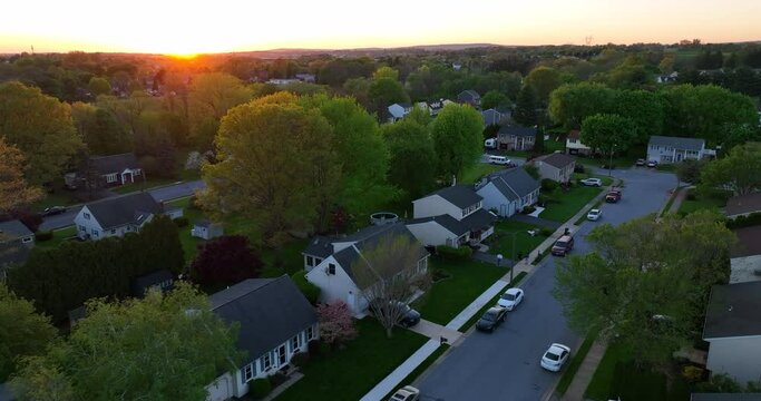 Cinematic aerial establishing shot of American neighborhood. Town in suburbs during magic hour sunset. Homes and houses line the streets in USA.