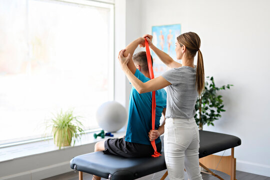 Modern rehabilitation physiotherapy woman worker with man client using red elastic
