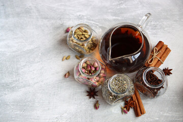 Obraz na płótnie Canvas Teapot and spices jars on light grey background with copy space. Different tea flavors on a table. Lavender, cardamom, cinnamon, rose, anise stars and clove top view photo. 