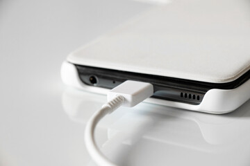 White mobile phone in a case lies on recharging on a white background, USB cable and phone close up, fast phone charging