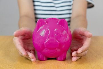 Woman hand holding pink piggy bank , investment concept , protection and security concept .